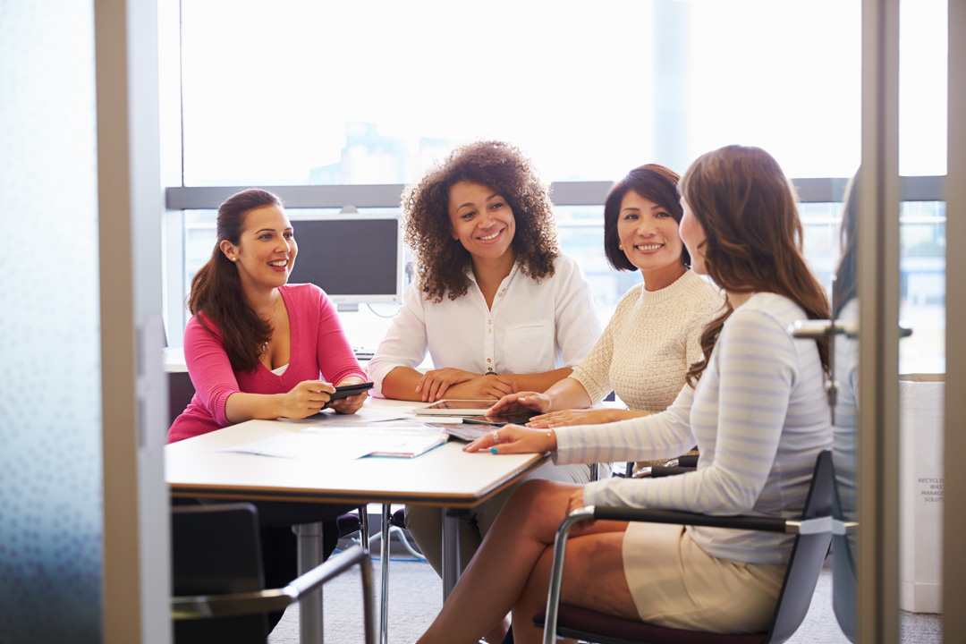 Vier Frauen sitzen für eine Besprechung in einem Schulungsraum oder Büro.